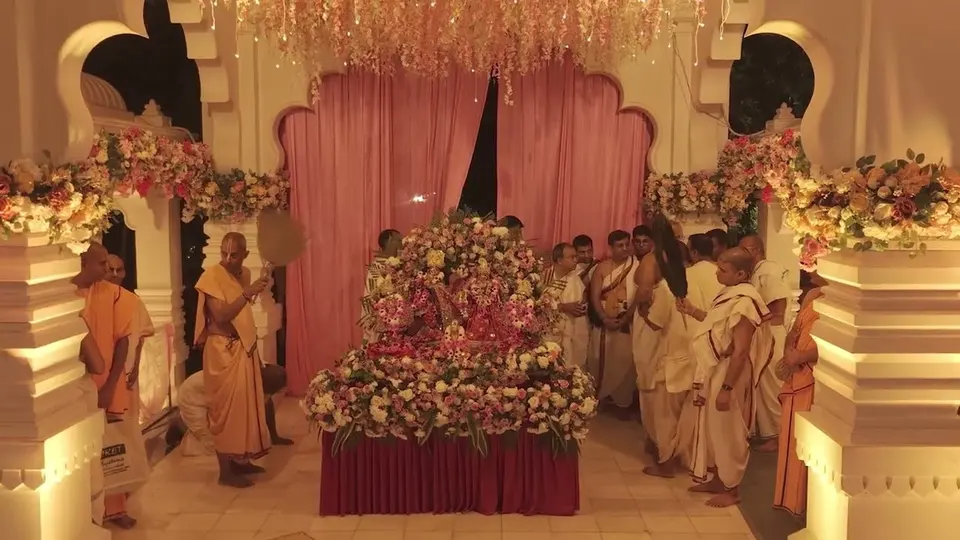 The deities on a flower-laden altar in the Mandir hall, devotees gathered on either side